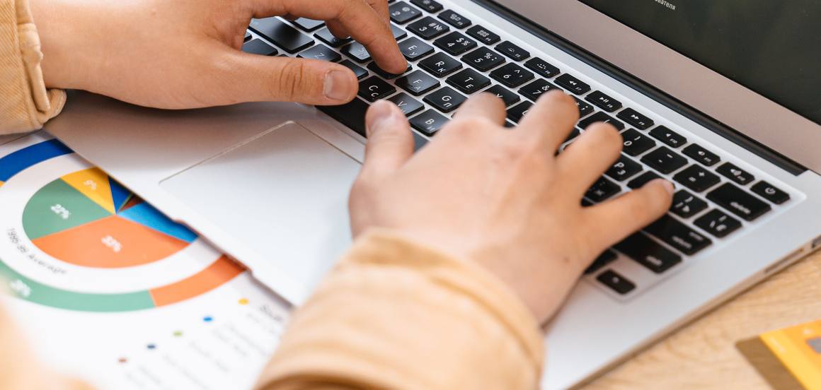Deux mains sur le clavier d’un ordinateur portable, un graphique posé sur la table